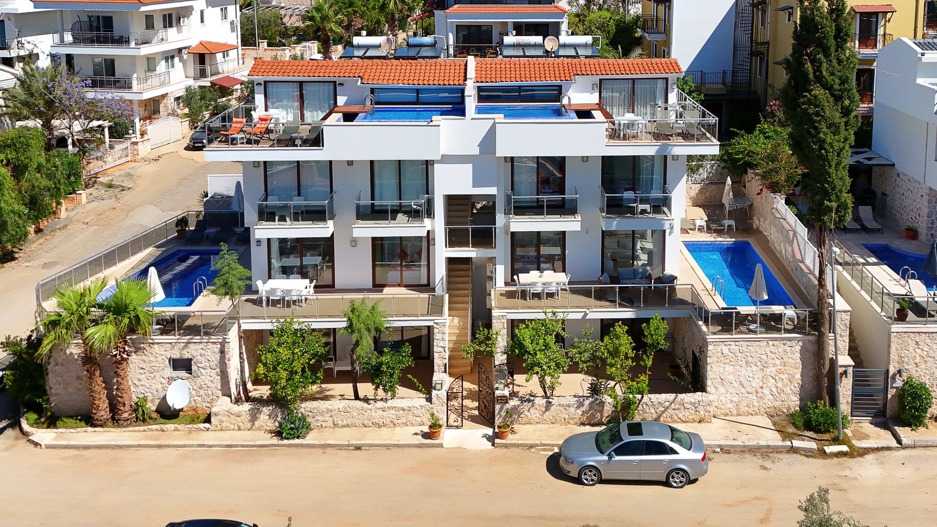 Çok katlı beyaz apart villanın ön cephesi, havuzları ve balkonları.
