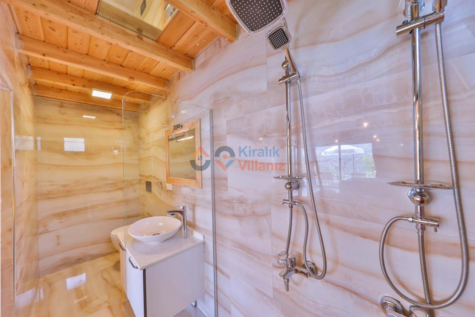 Mermer görünümlü duvarlara sahip duşakabin, krom batarya ve beyaz banyo dolabı.