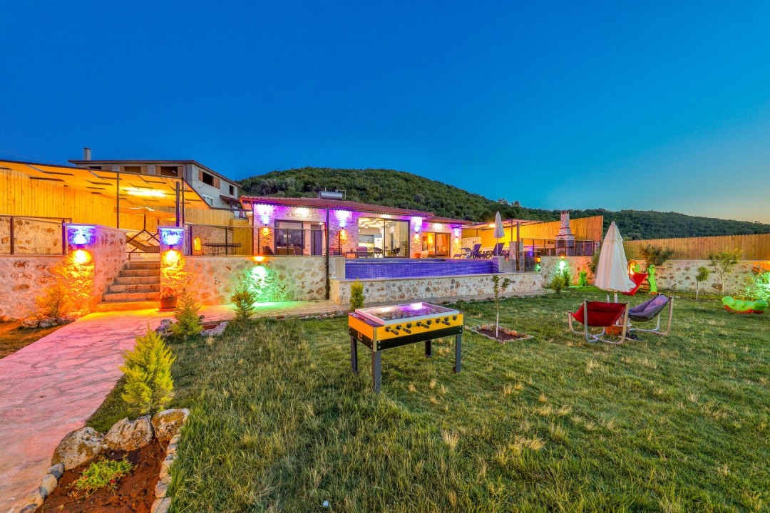 Akşam vakti ışıklandırılmış havuzu, bahçesi ve langırt masası olan taş villa.