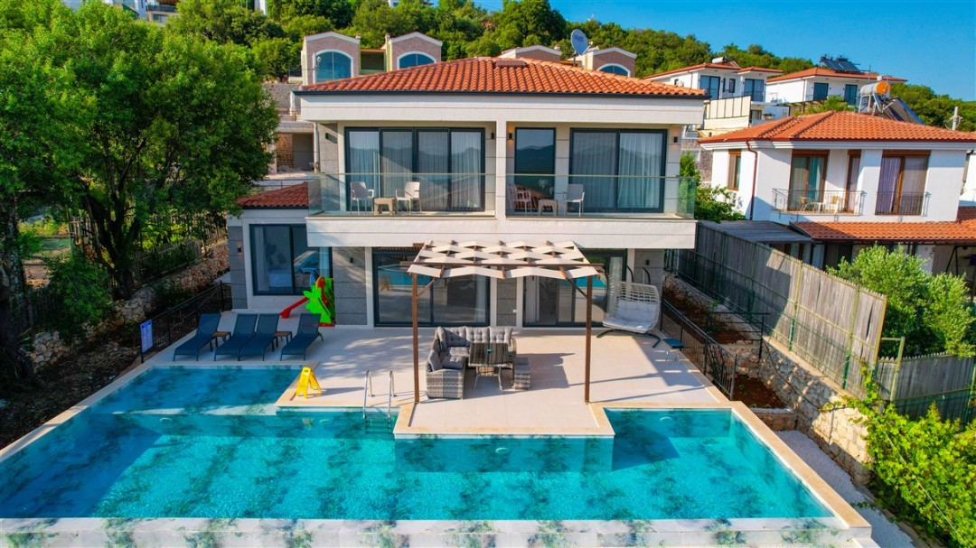 Önünde havuz ve şezlonglar olan, balkonu ve terasında oturma grubu bulunan iki katlı villa.