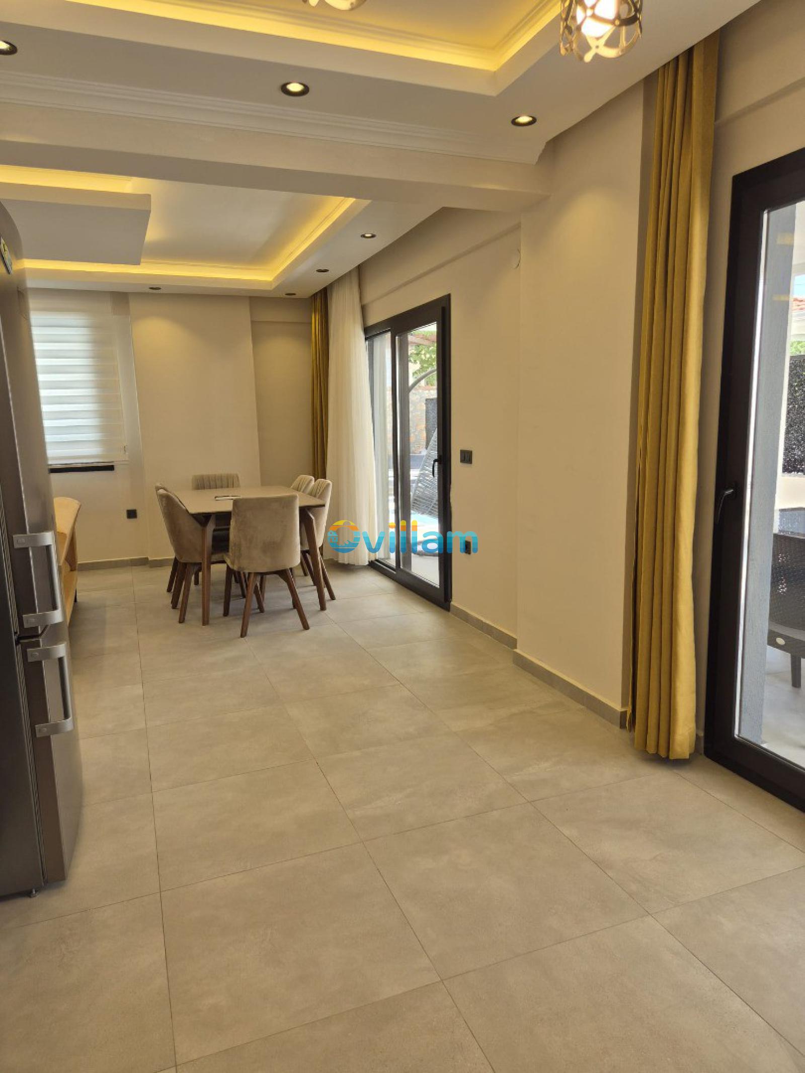 Modern aydınlatmalı, bej sandalyeli yemek masası bulunan sade bir iç mekân.