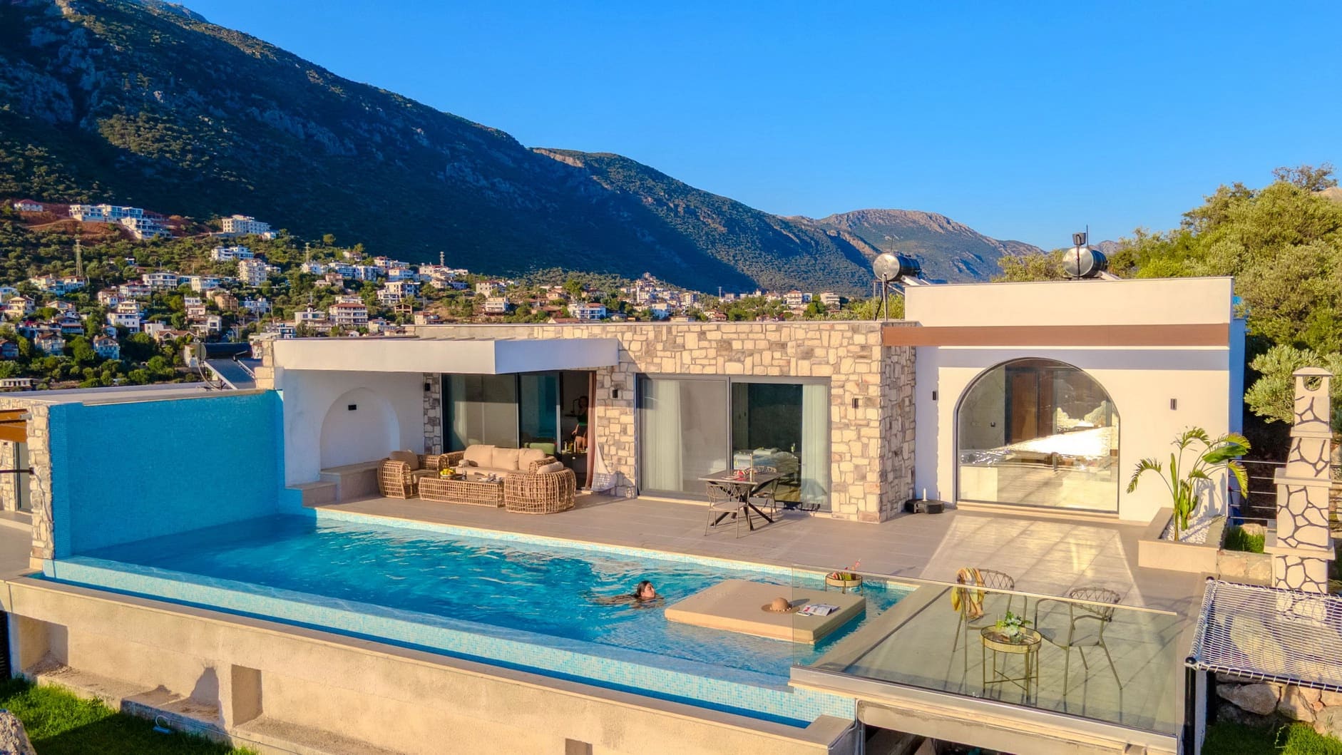 Dağ ve yerleşim manzaralı modern villanın önünde sonsuzluk havuzu var.