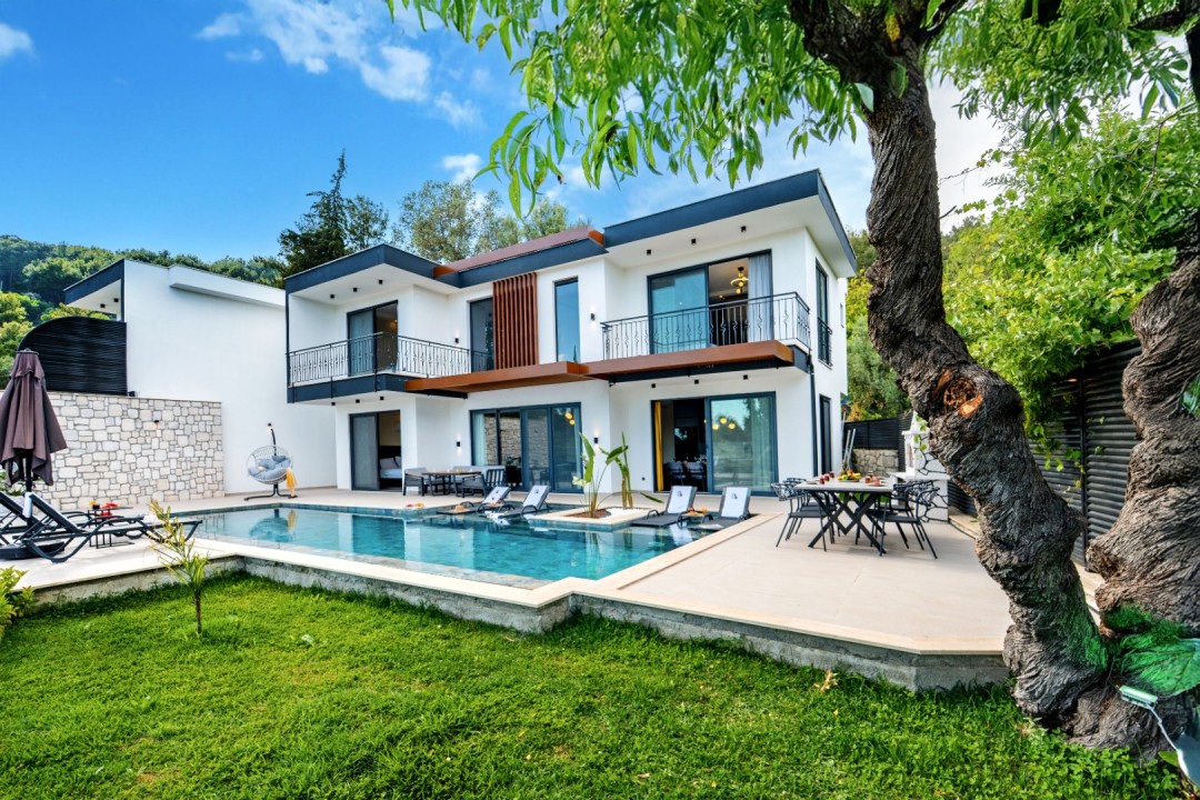 Önünde havuz, şezlonglar ve yemek masası olan iki katlı beyaz villa.