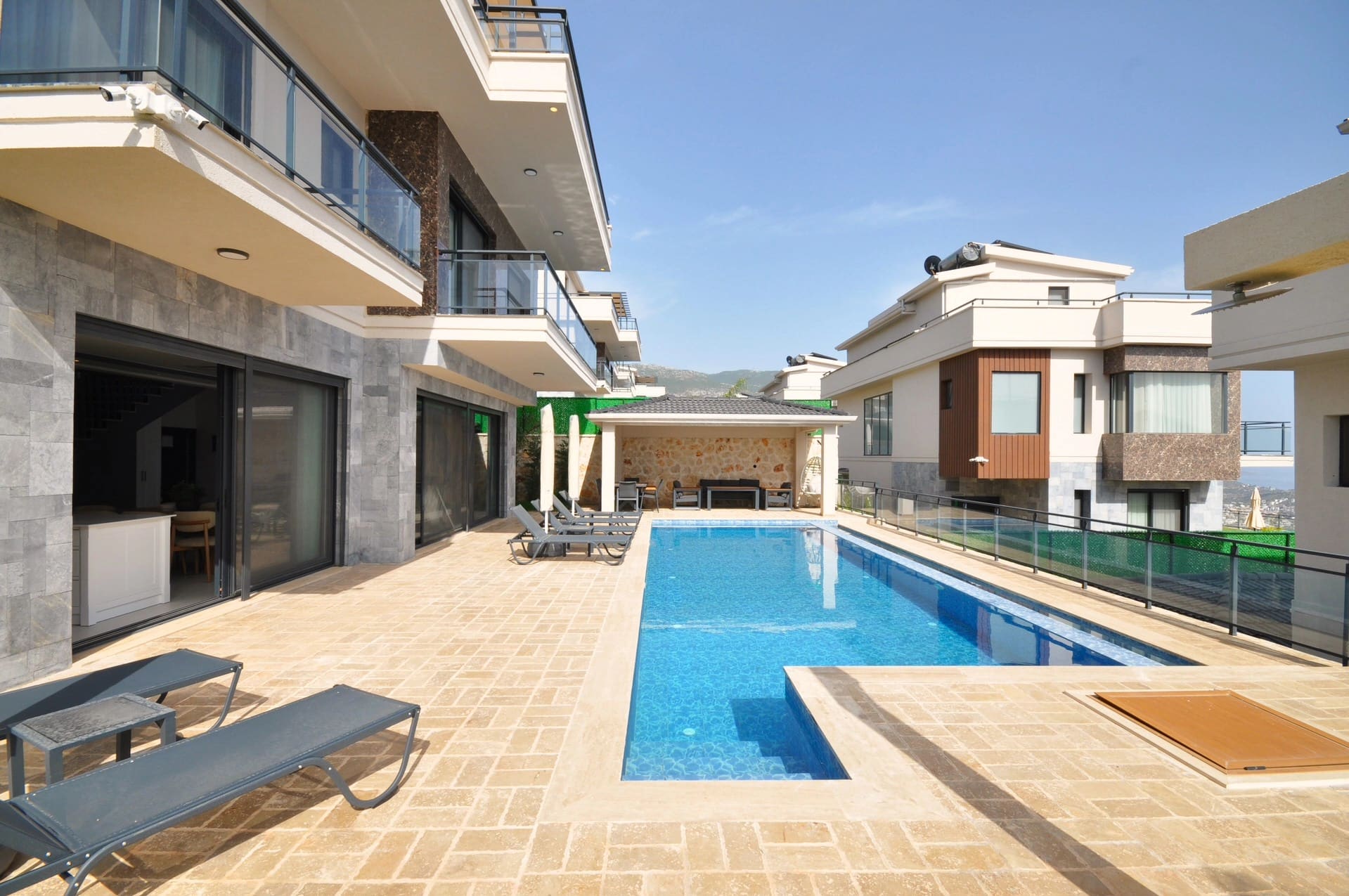 Geniş havuz terası, şezlonglar ve modern mimarili çok katlı villa binaları.