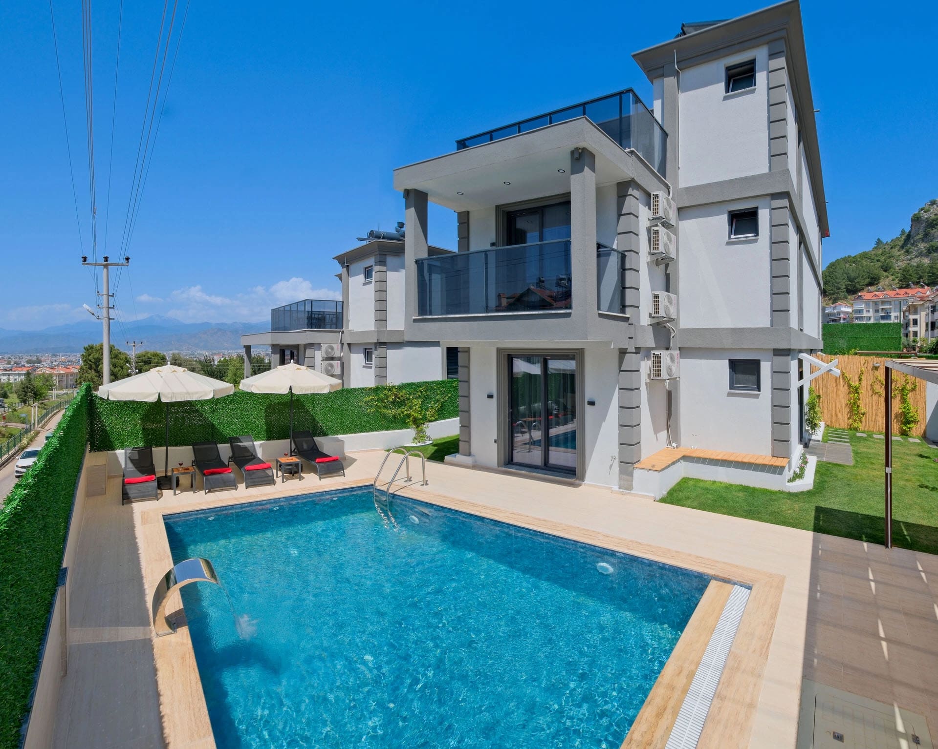 Güneş şemsiyeleri, şezlonglar ve özel yüzme havuzu bulunan villa dış cephesi.