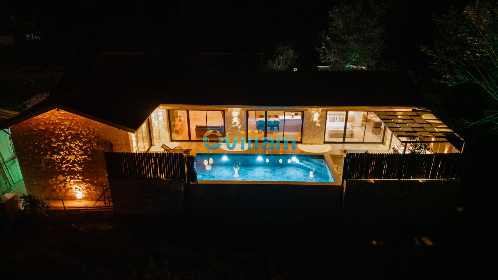 Geceleri aydınlatılmış taş villa, havuz ve teras alanı.