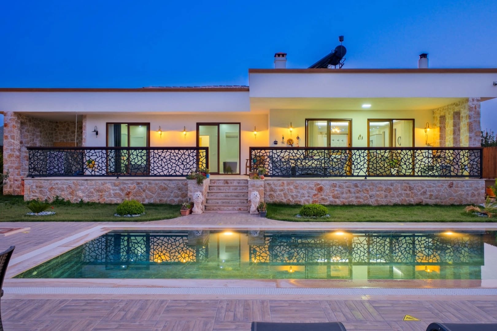 Gece aydınlatılmış, taş kaplamalı dış cepheye ve önünde havuz bulunan modern villa.