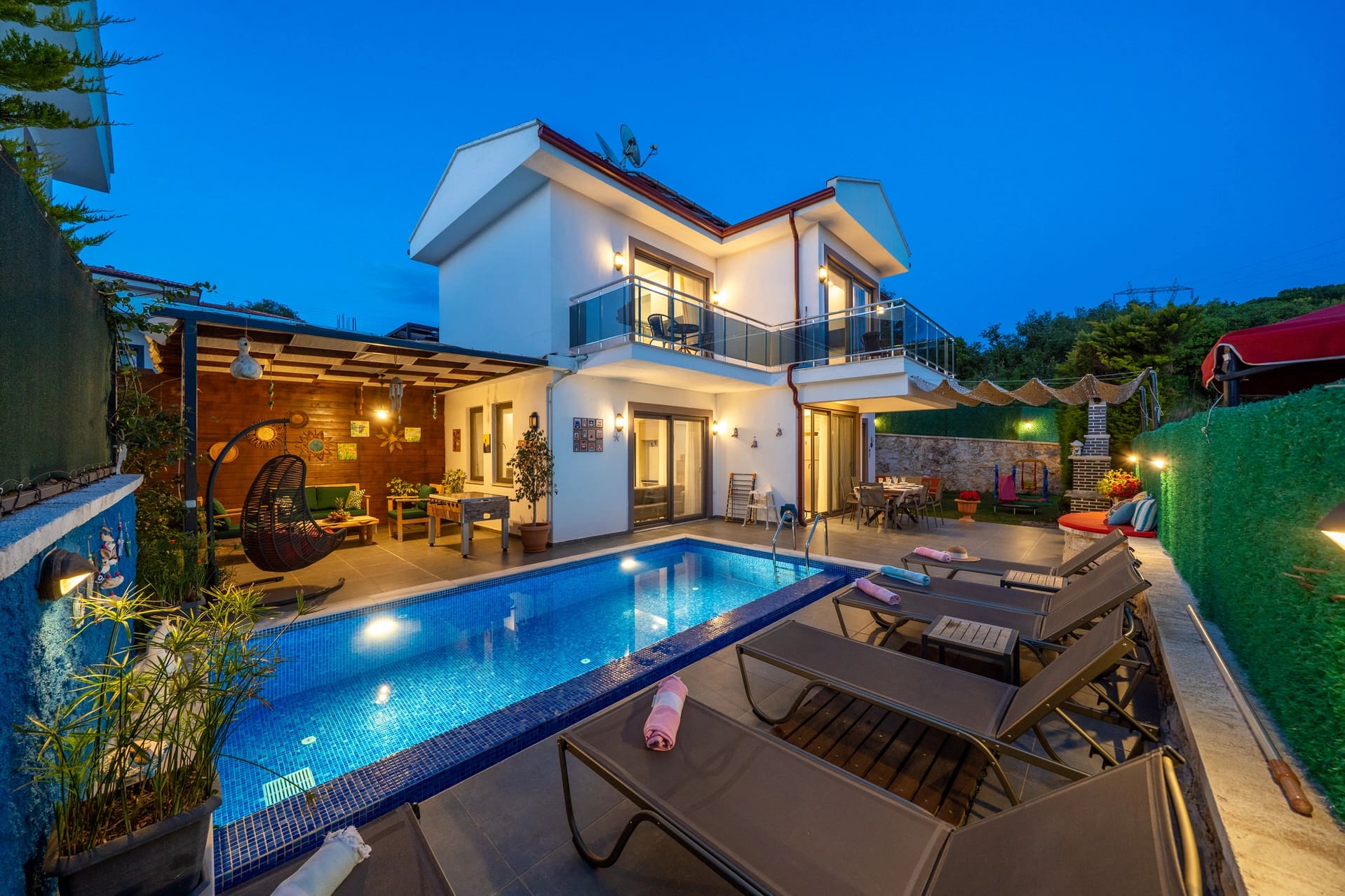 Akşam aydınlatmalı havuz kenarında şezlonglar ve iki katlı villa.