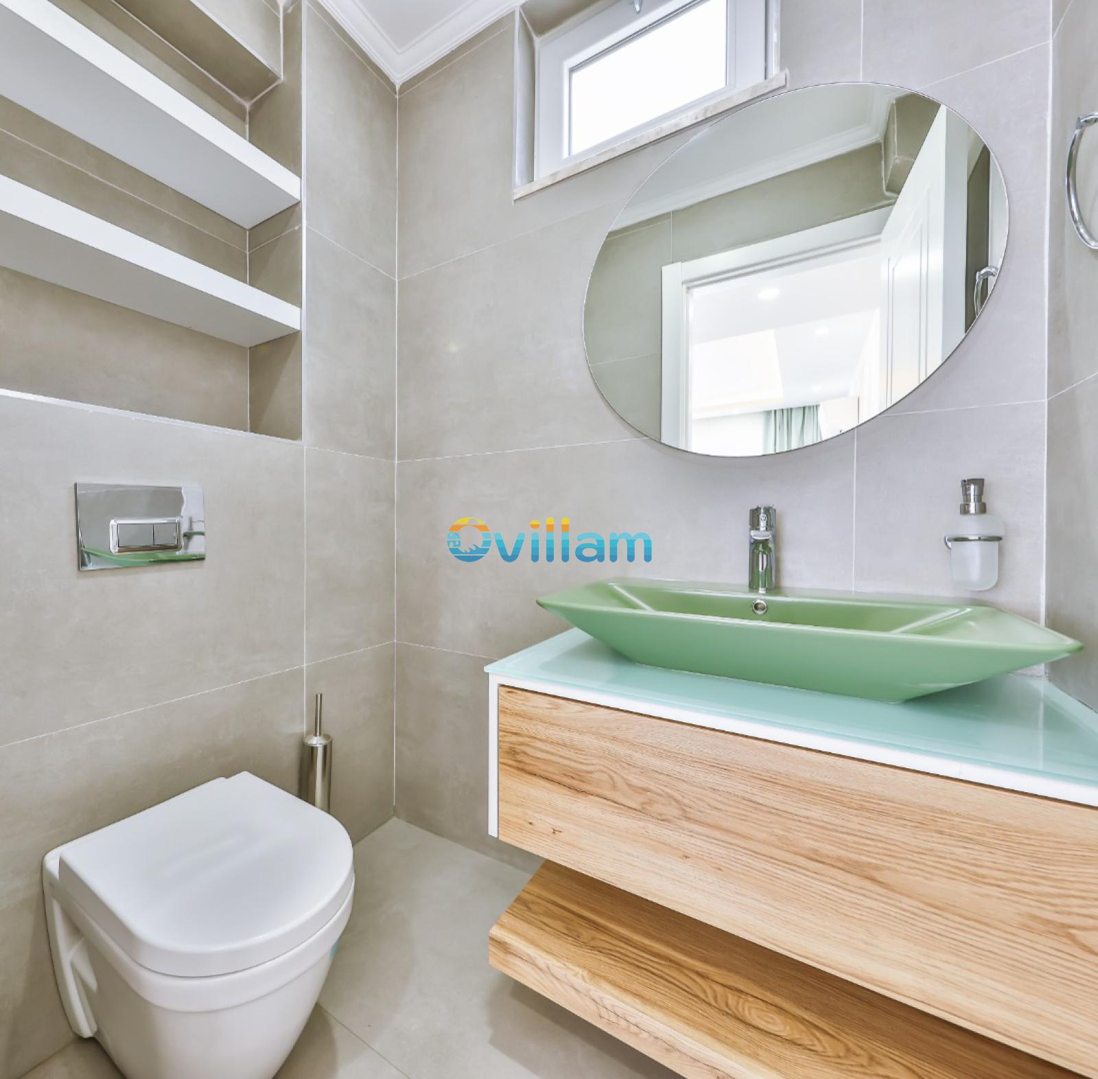 Bej fayanslı, oval aynalı, yeşil lavabolu ve ahşap dolaplı modern banyo.
