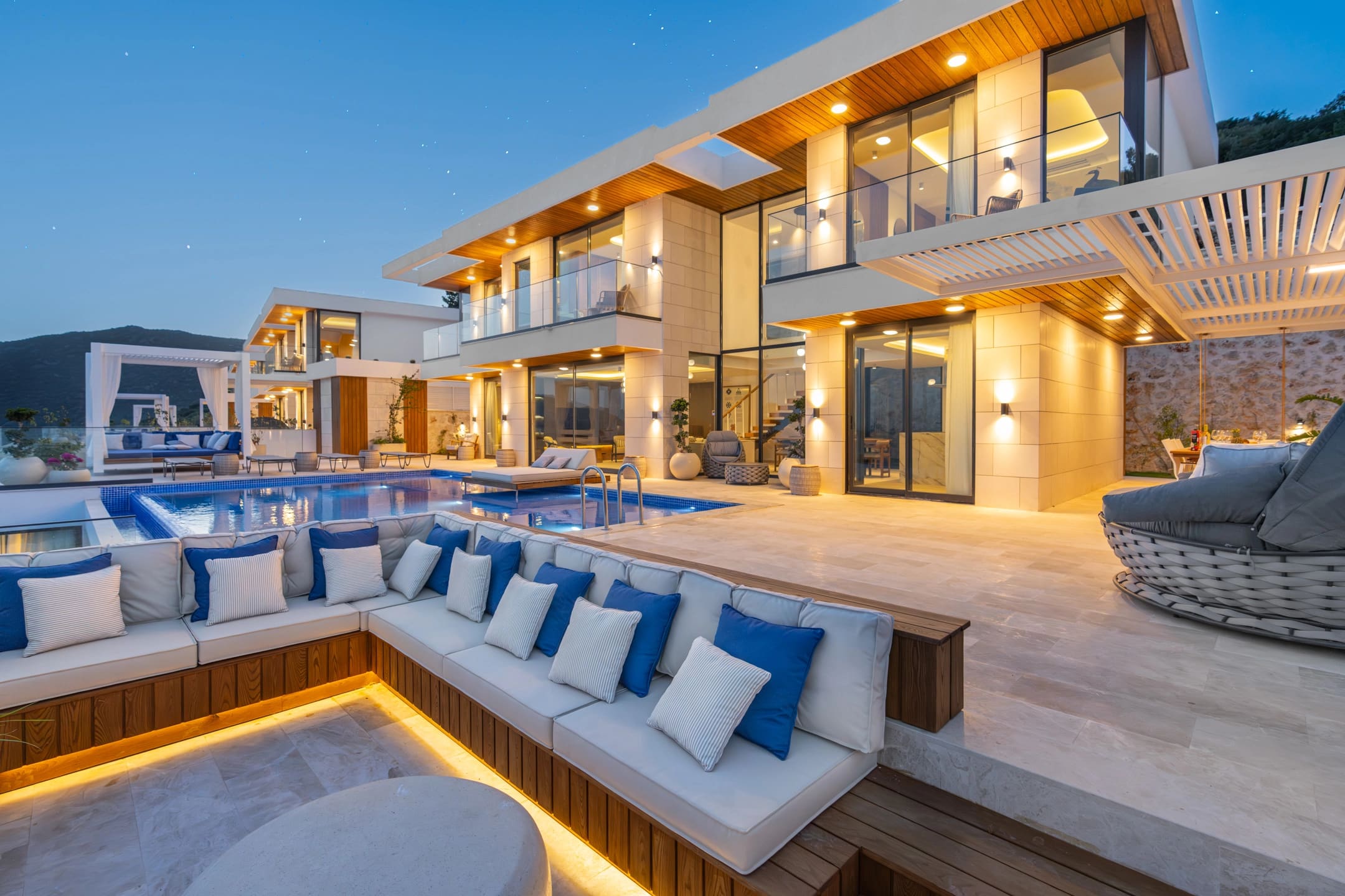 Akşam vakti havuz başındaki oturma alanları ve aydınlatılmış modern villa dış cephesi.