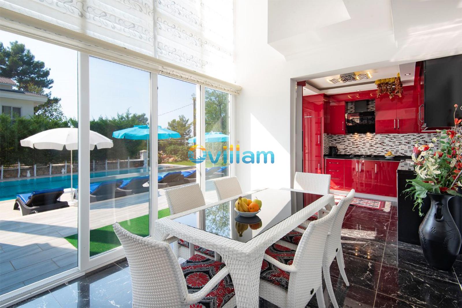 Cam pencereler önünde yemek masası ve arka planda havuz görünen yemek alanı.