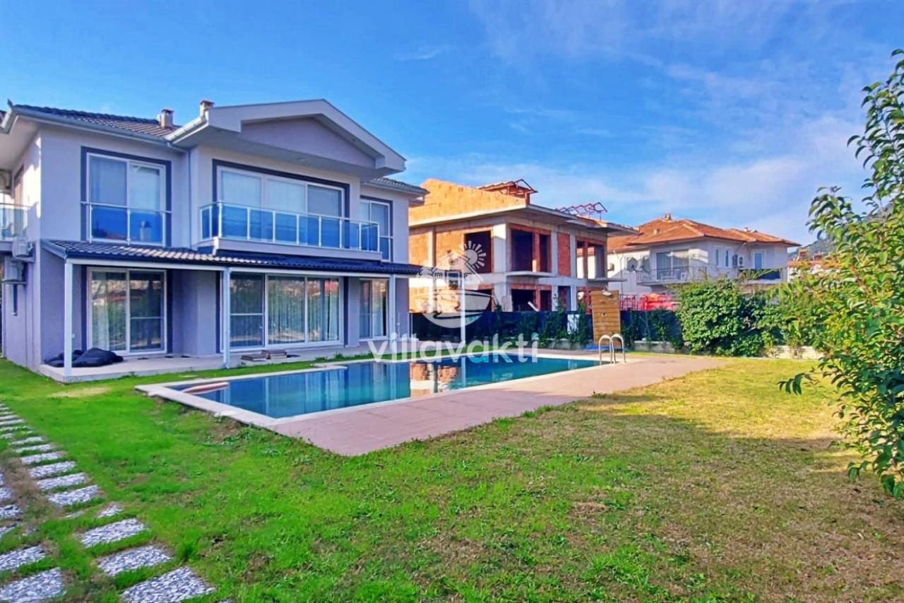 Önünde yüzme havuzu bulunan, iki katlı, gri dış cepheli modern bir villa.