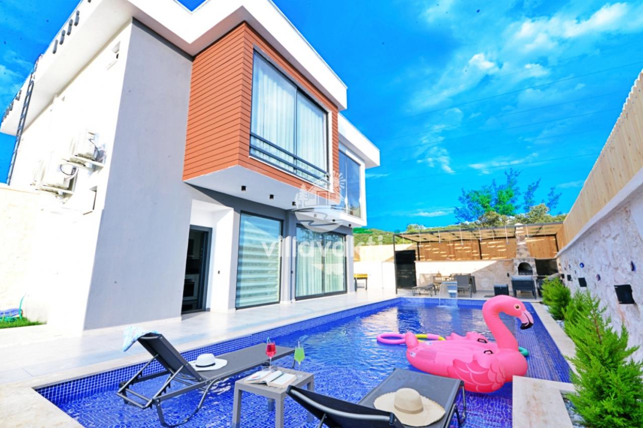 Flamingo deniz yatağı bulunan havuz, şezlonglar ve modern mimariye sahip villa dış cephesi.