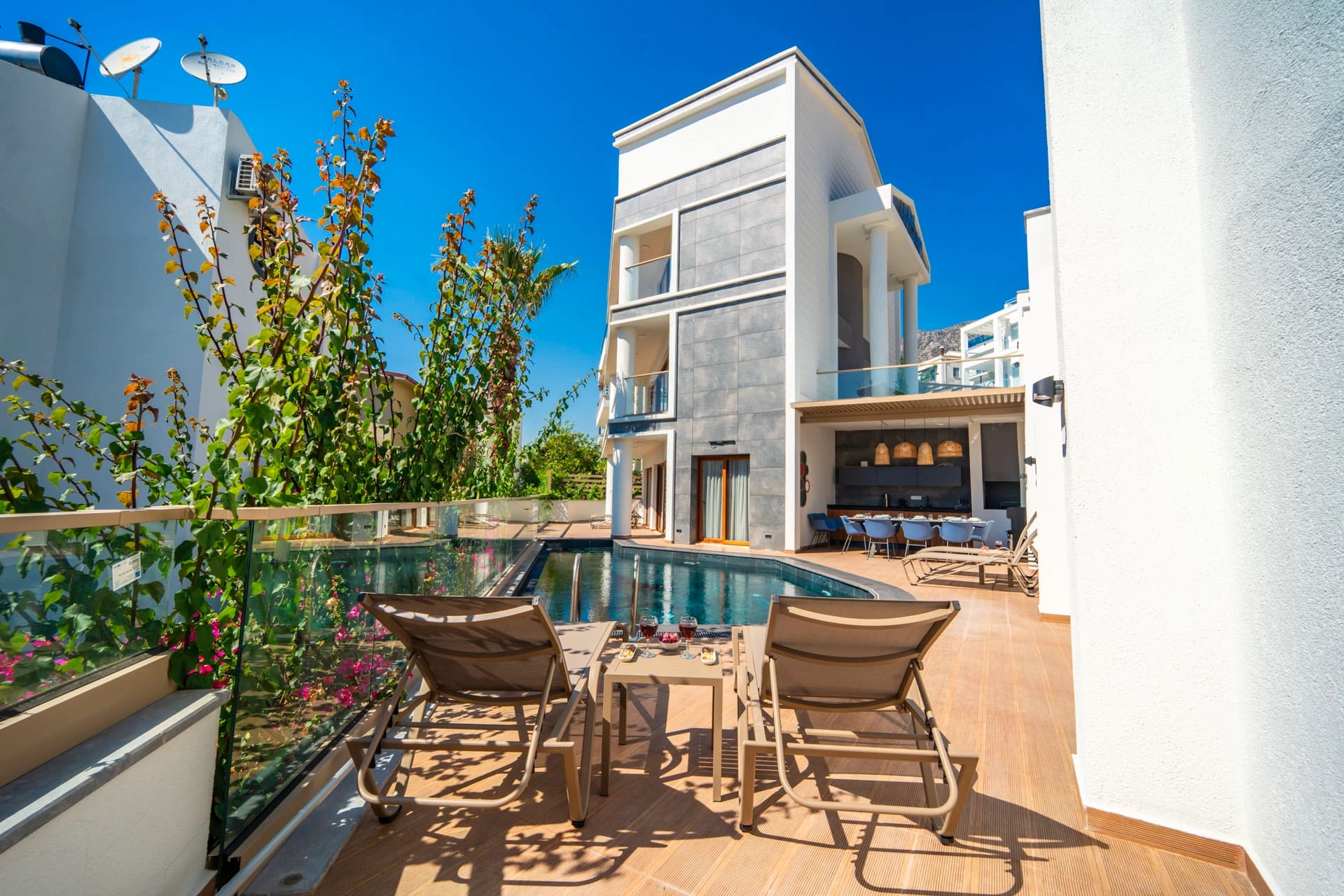 Havuz kenarında şezlonglar ve arka planda modern villa.