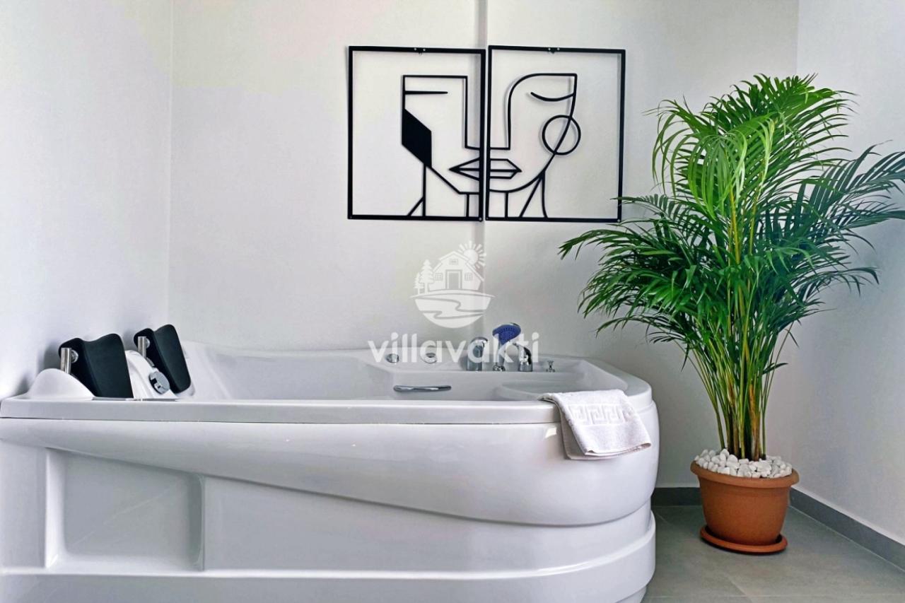 Beyaz jakuzi ve yanında yeşil bitki bulunan banyo.