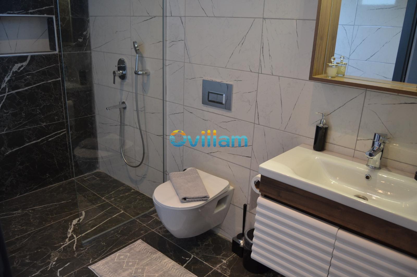 Modern banyo içerisinde cam bölmeli duş alanı, asma klozet ve aynalı lavabo ünitesi.