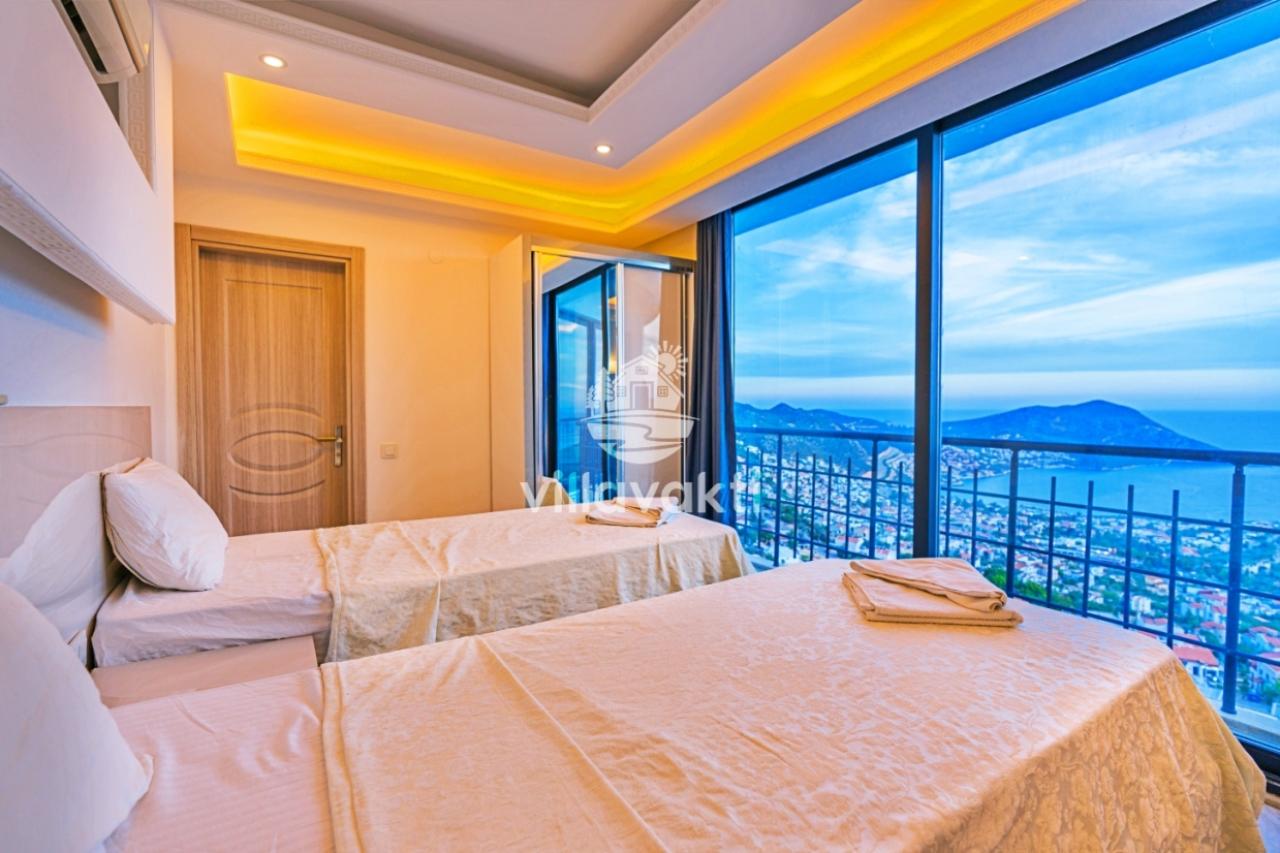 İki tek yataklı, balkon kapısından panoramik deniz ve dağ manzarası görünen yatak odası.