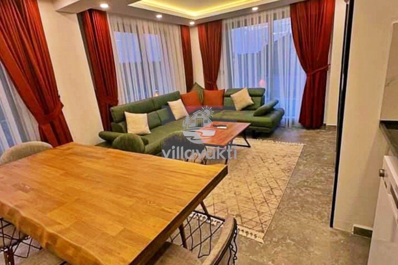 Kırmızı perdeli, yeşil koltuk takımı ve ahşap yemek masası bulunan oturma odası.