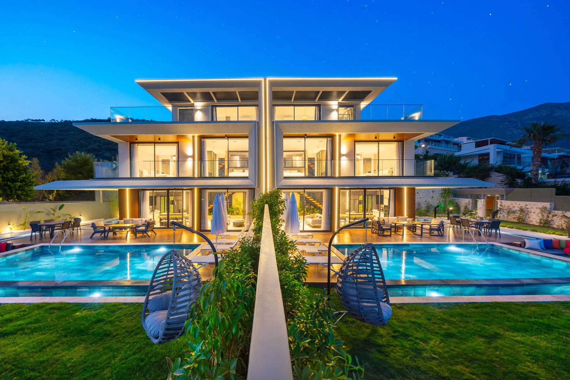 Gece aydınlatılmış modern villa, havuz ve bahçedeki asma koltuklar ile dış görünüm.