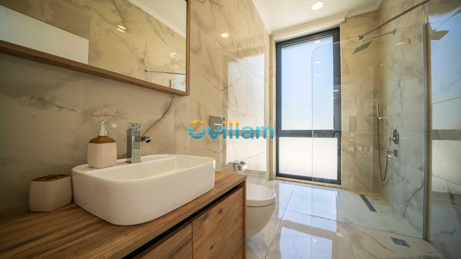 Mermer kaplı modern banyo, duşakabin, lavabo ve geniş bir pencere.
