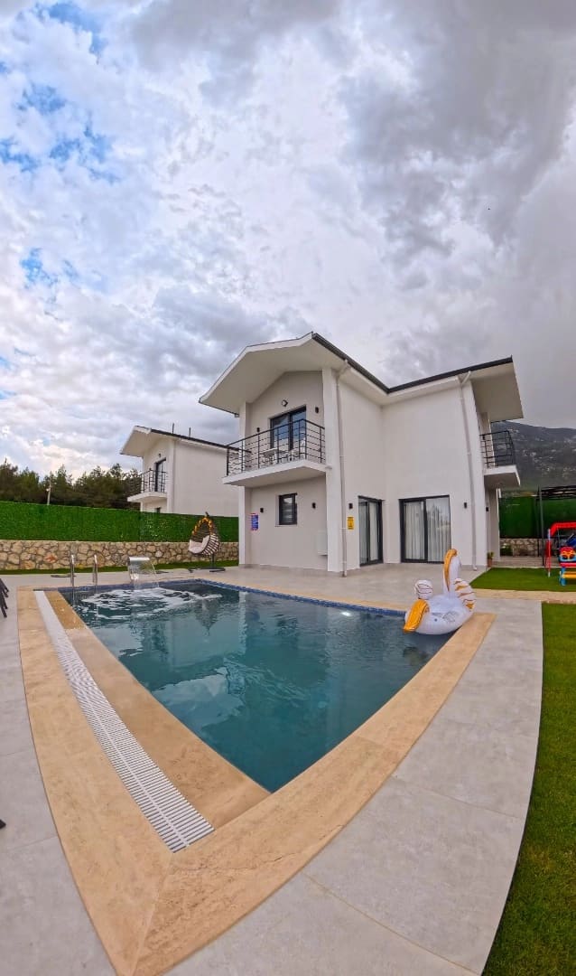 Beyaz dış cepheli iki katlı villa ve önünde içinde kuğu figürlü deniz yatağı bulunan yüzme havuzu.