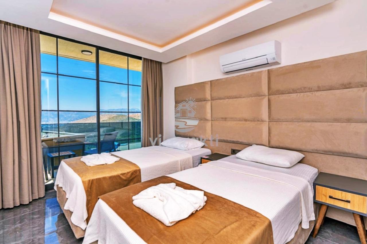 İki tek kişilik yatak, bej renkli yatak başlığı ve cam balkon kapısı olan yatak odası.