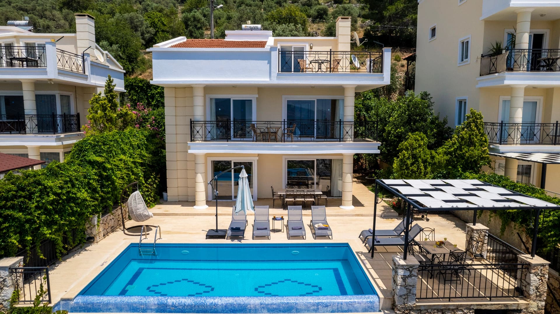 Havuzlu, şezlonglu, balkonlu ve bahçeli üç katlı modern villa dış cephesi.