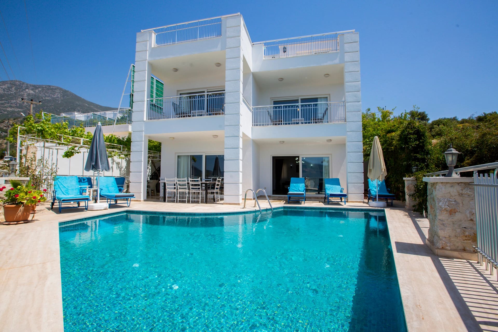 Önünde özel havuzu, güneş şezlongları ve yemek masası bulunan iki katlı beyaz modern villa.