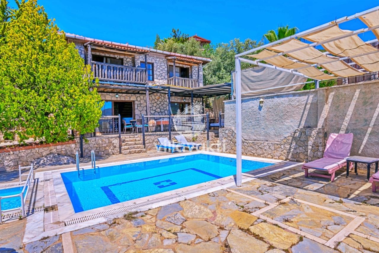 Taş duvarlı iki katlı villa, önünde şezlonglar bulunan özel yüzme havuzu ve bahçe.