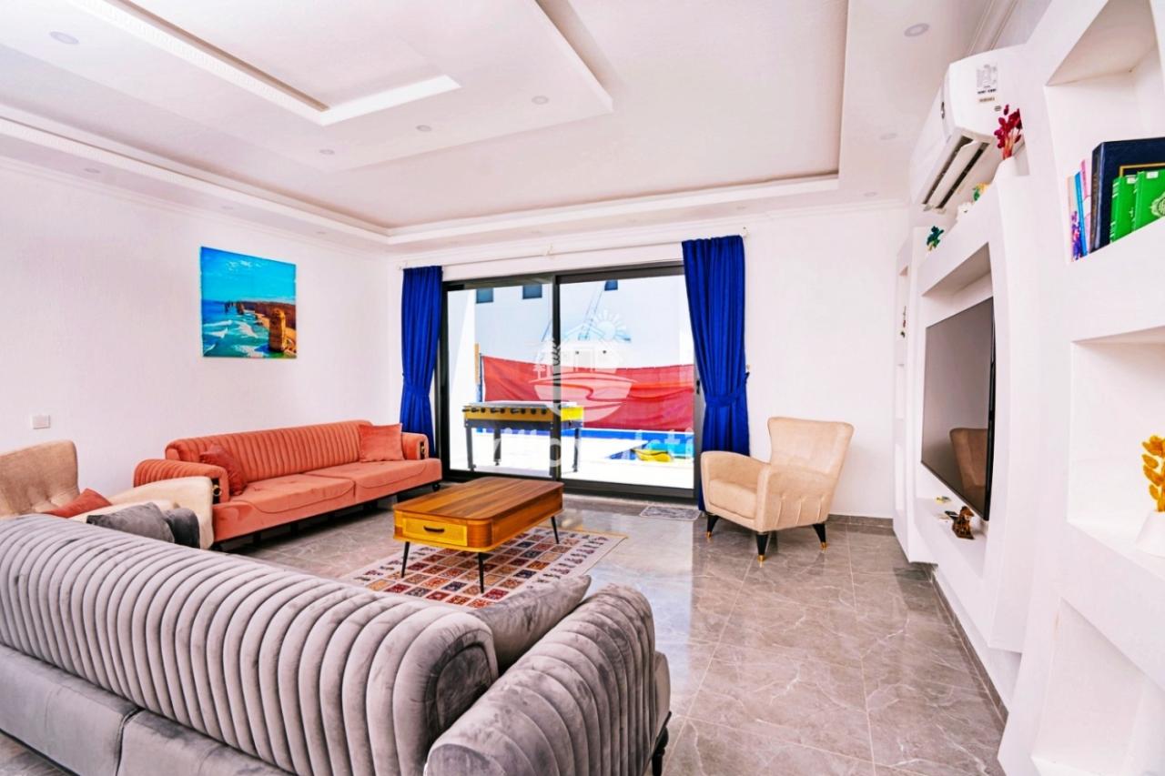 Modern salon içerisinde gri ve kiremit rengi koltuk takımı, orta sehpa ve karşıda televizyon ünitesi.