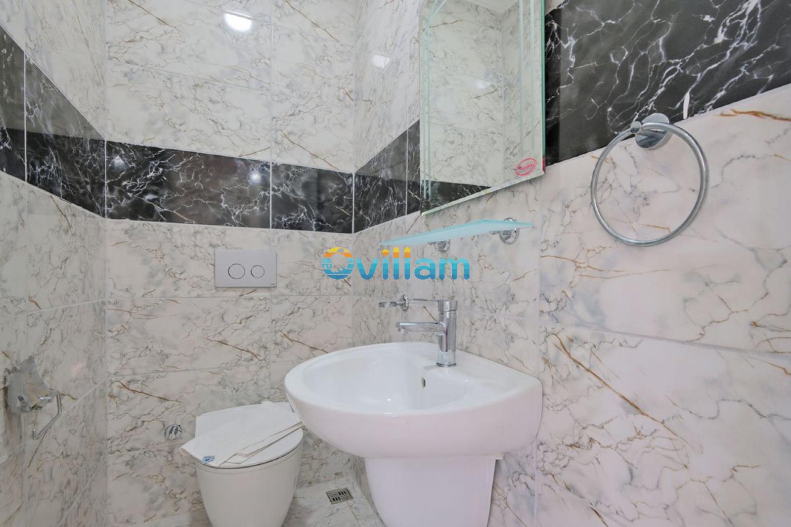 Mermer görünümlü duvar kaplamalı küçük banyo, beyaz lavabo ve klozet.