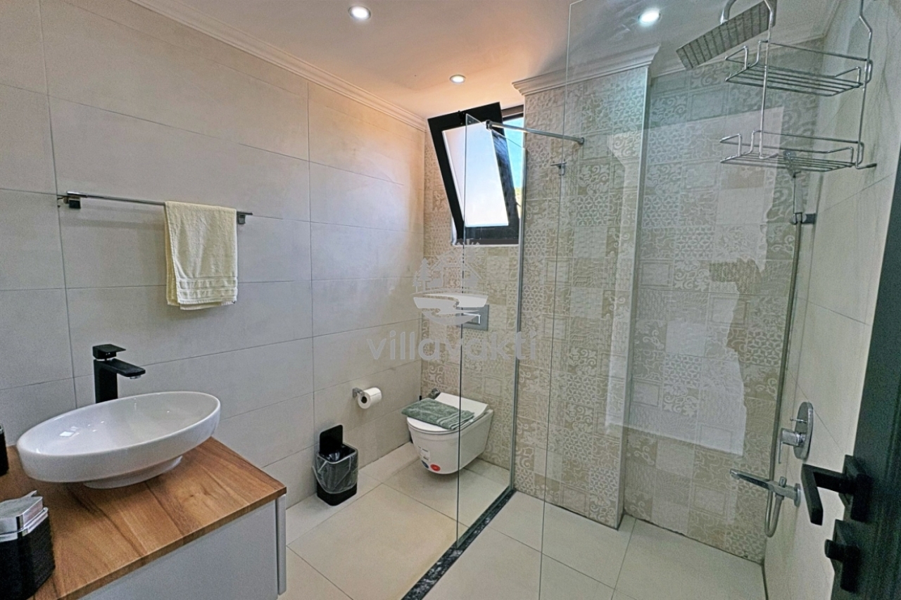 Modern banyoda duşakabin, lavabo, klozet ve desenli fayans kaplı duvarlar bulunuyor.