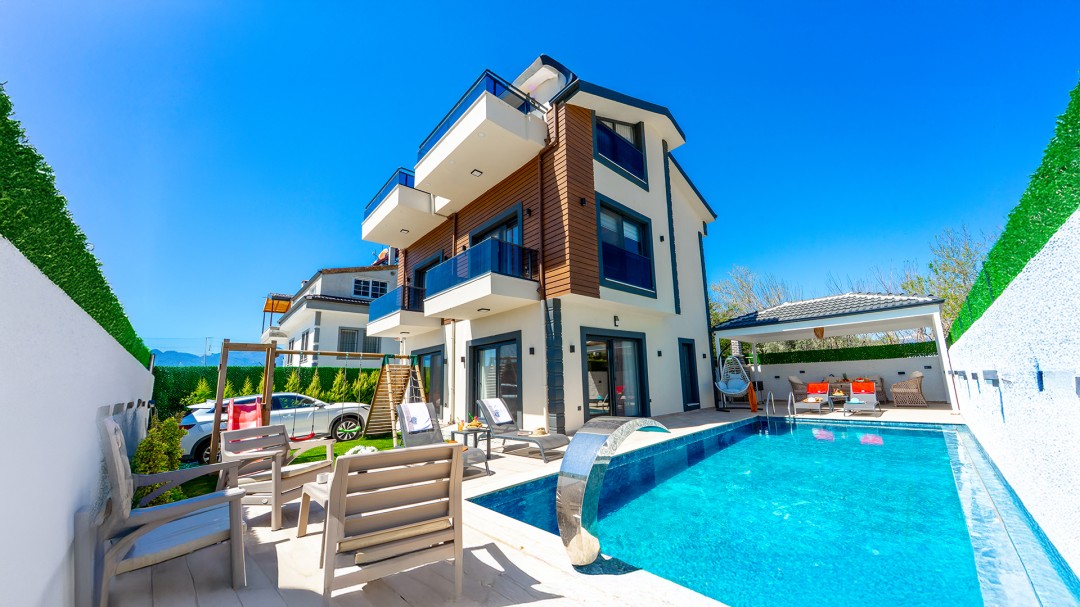 Gündüz vakti havuzu, şezlongları ve bahçesinde çocuk parkı olan çok katlı lüks villa.