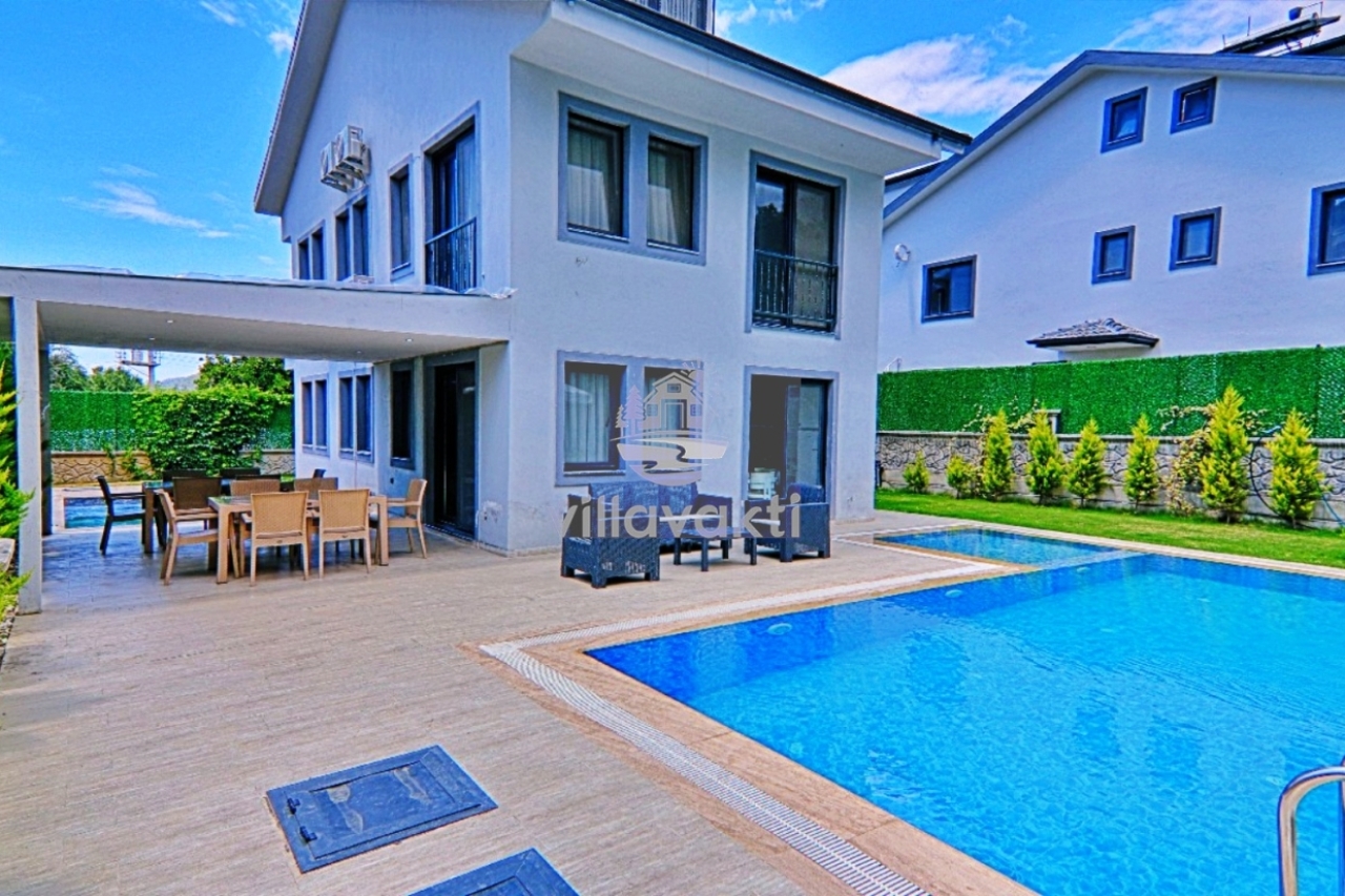 Bahçesinde özel havuz ve yemek masası bulunan iki katlı beyaz villa.