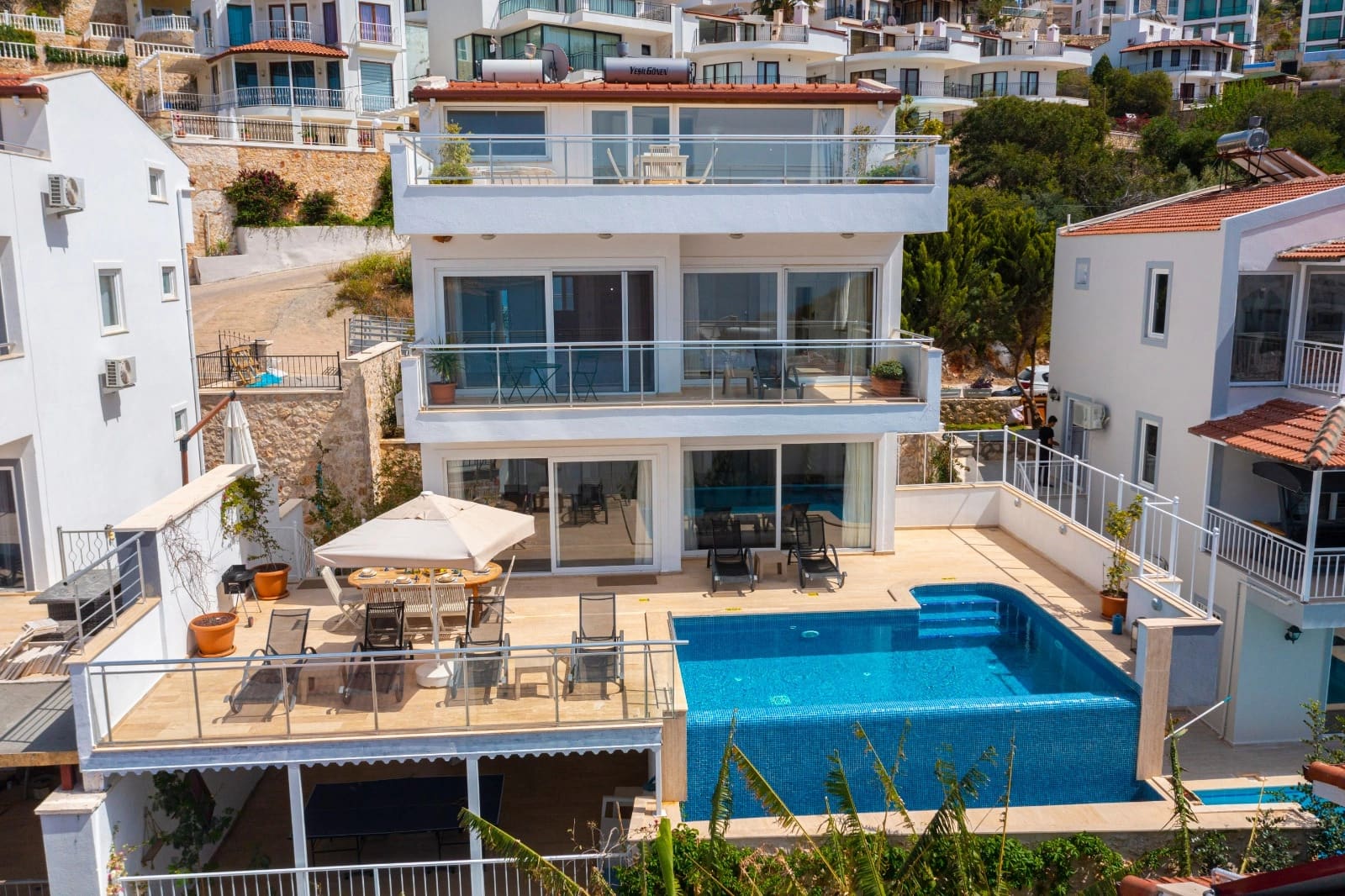 Önünde yüzme havuzu ve şezlonglar bulunan beyaz katlı villa