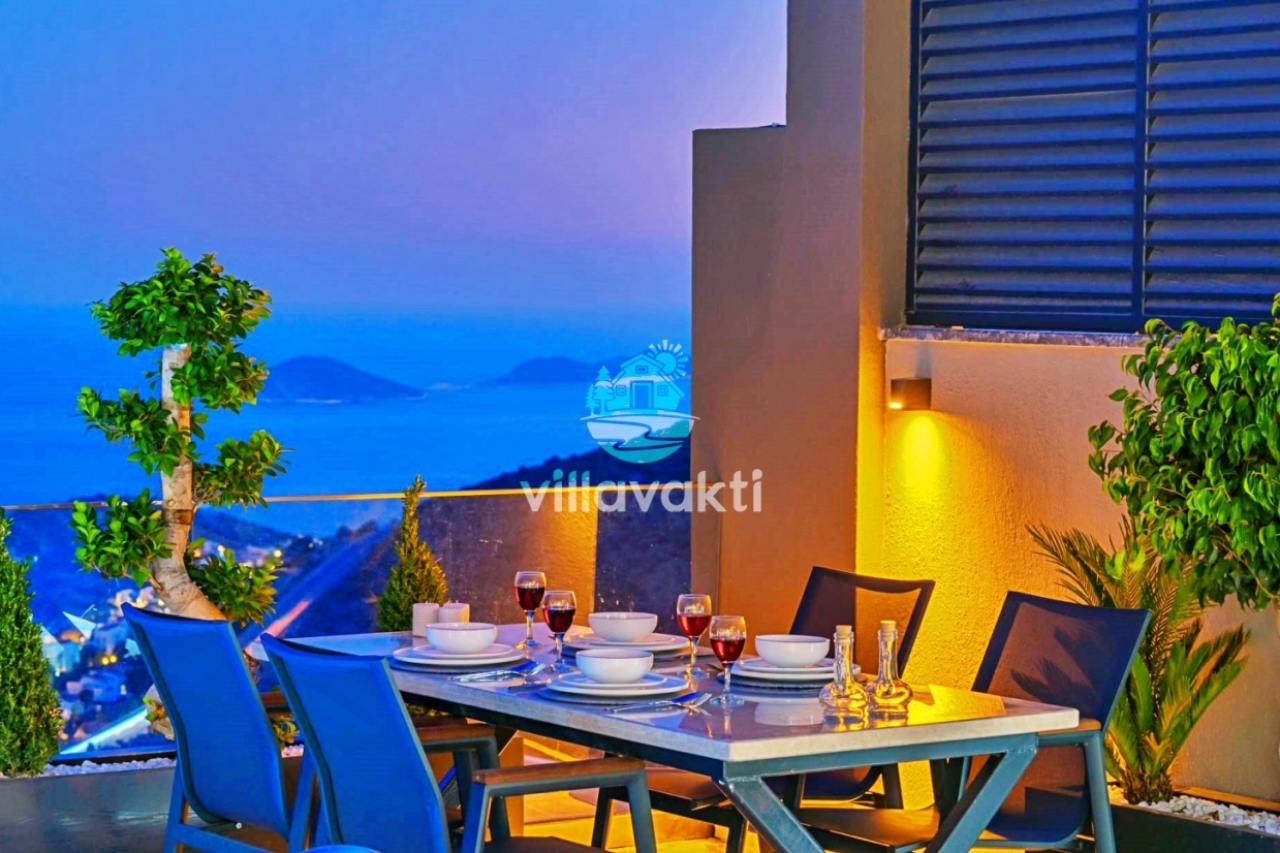 Gün batımında deniz manzaralı terasta kurulu akşam yemeği masası ve sandalyeler.