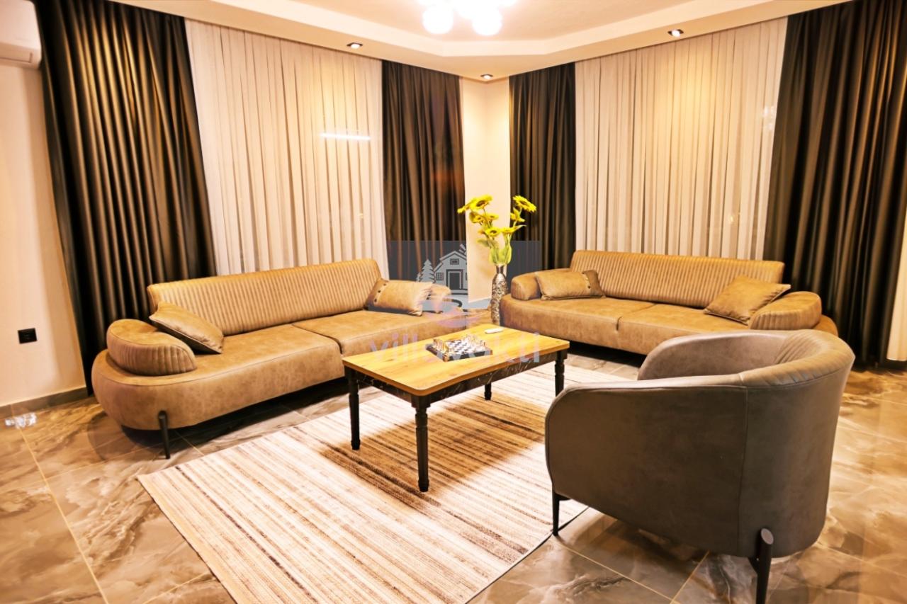 Kahverengi koltuk takımı, ahşap sehpa ve desenli halı bulunan geniş salon.