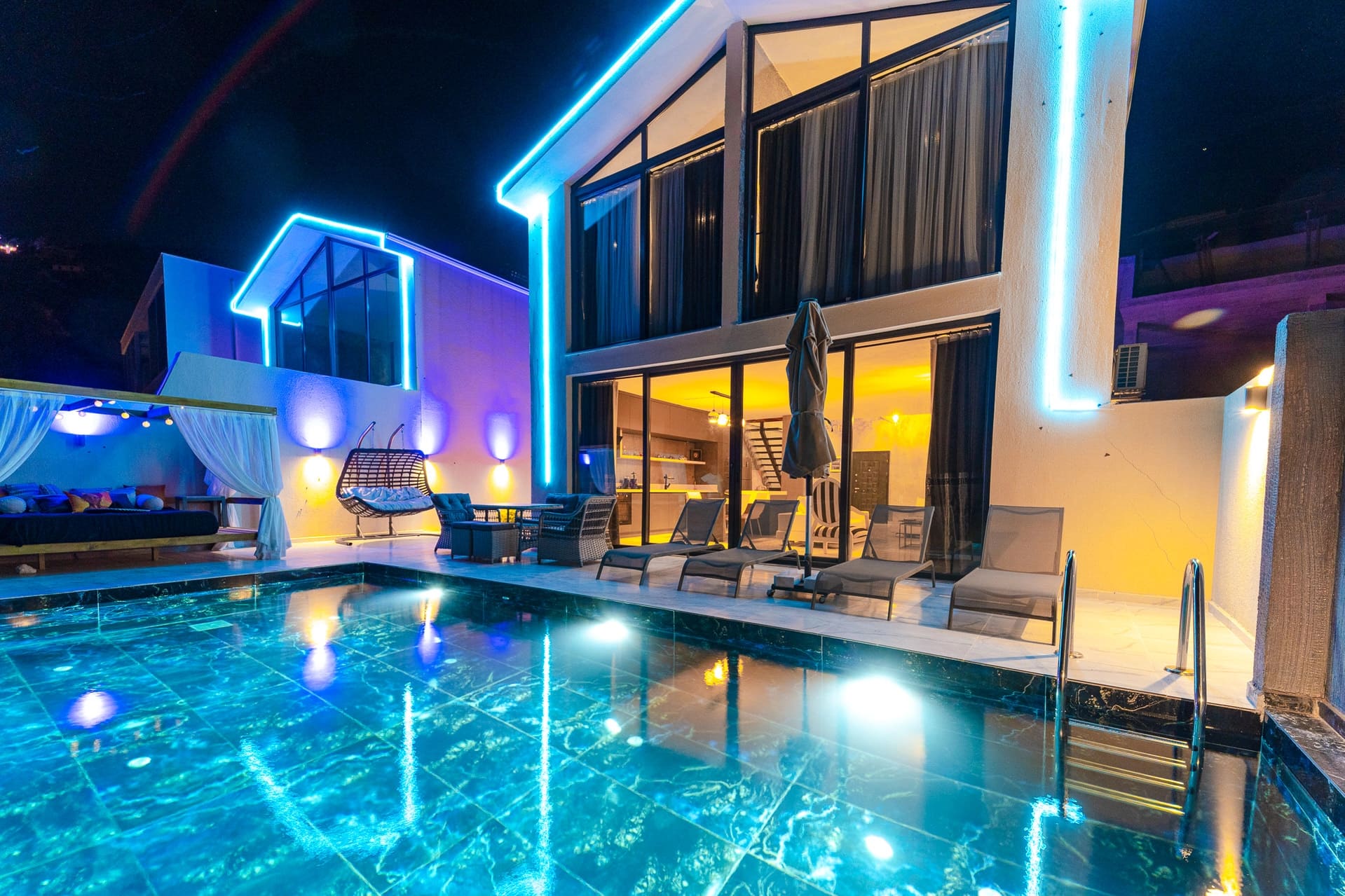 Mavi LED ışıklarla aydınlatılmış iki katlı modern villa, gece vakti ışıklandırılmış yüzme havuzu.