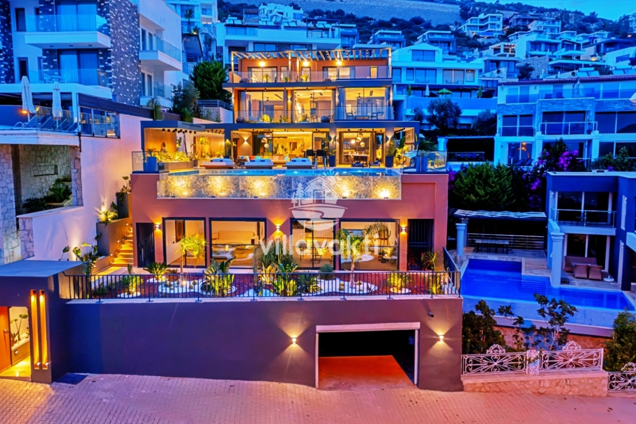 Akşam ışıklandırılmış, yamaçta yer alan çok katlı modern villanın dış cephesi ve havuz alanı.