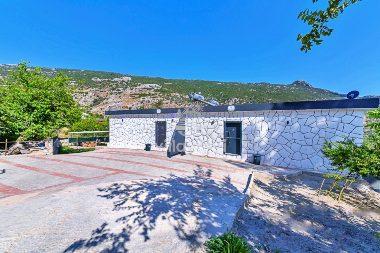 Taş desenli beyaz dış cepheye ve park alanına sahip dağ manzaralı tek katlı villa.