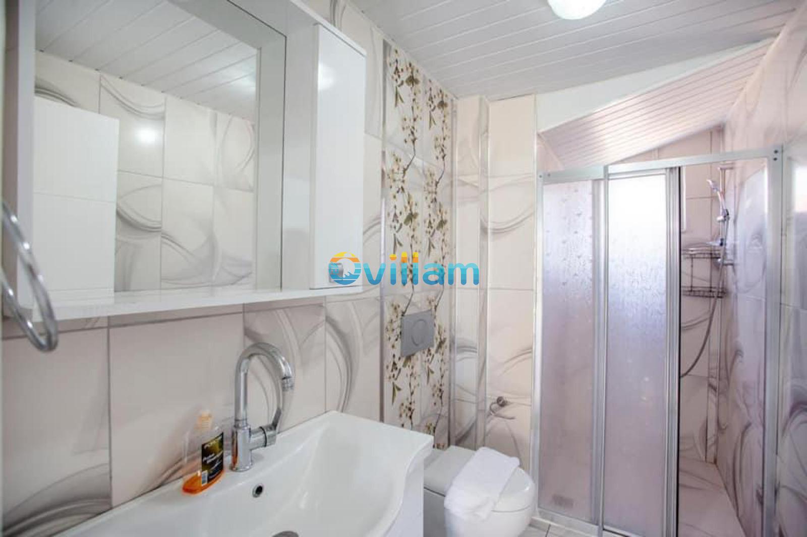 Aynalı üst dolap, lavabo, klozet ve cam duşakabinden oluşan fayans kaplı banyo.