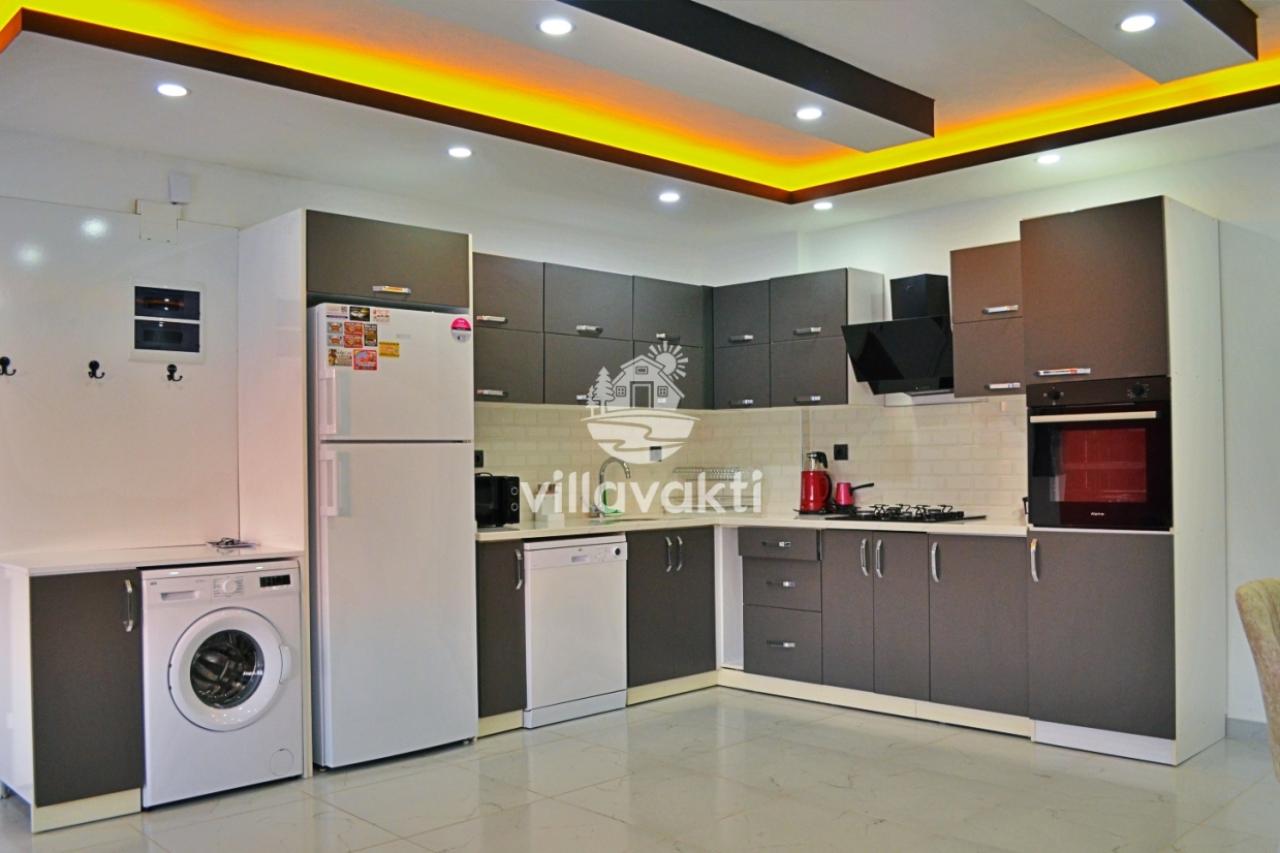 Beyaz ve gri dolaplı, ankastre fırın ve buzdolabının bulunduğu modern mutfak.