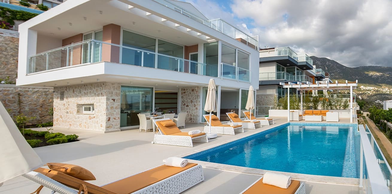 Geniş havuz kenarında şezlonglar ve havuz bulunan modern iki katlı villa.