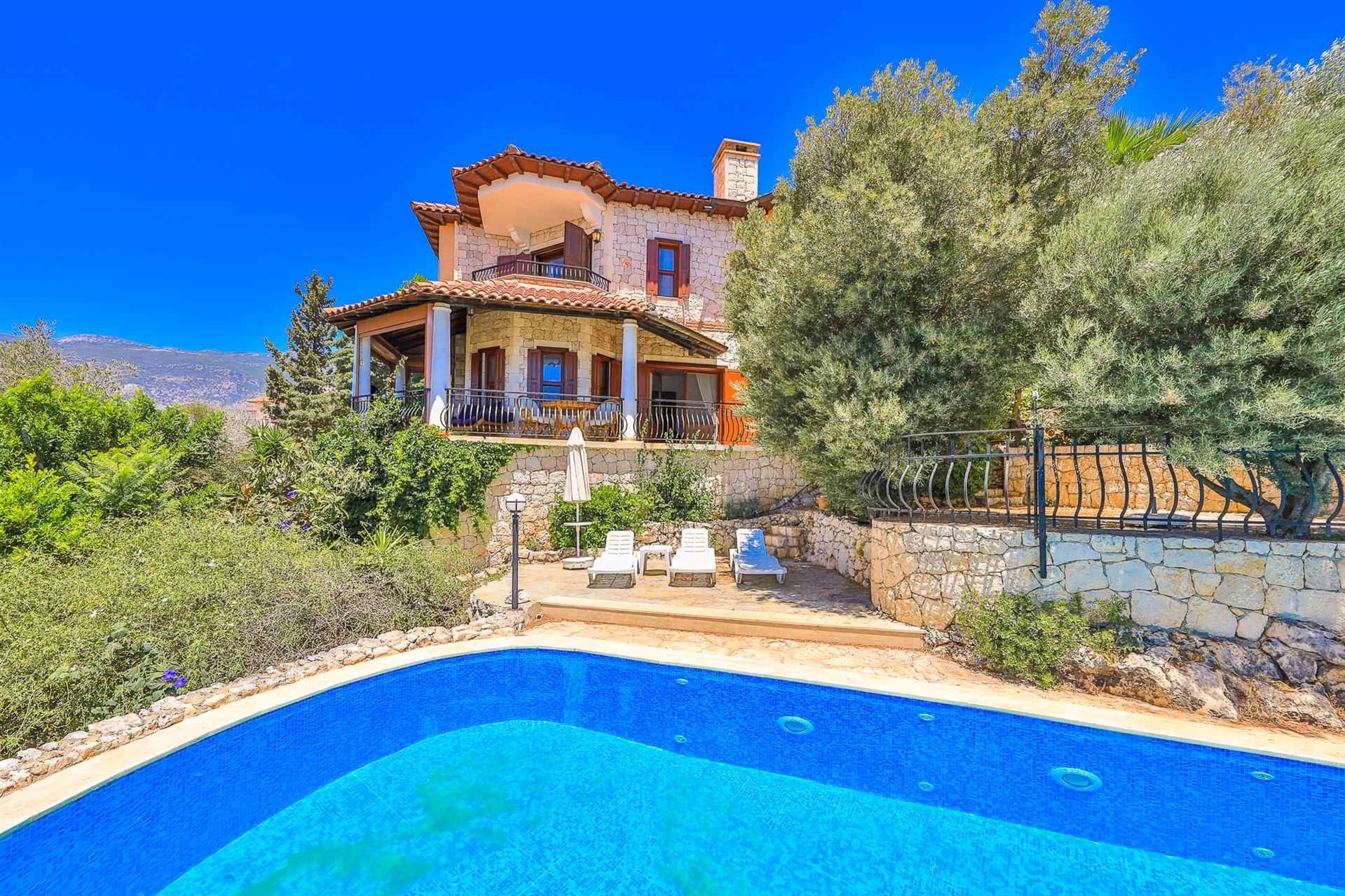 Ağaçlar arasında taş villa ve önünde açık havuz.