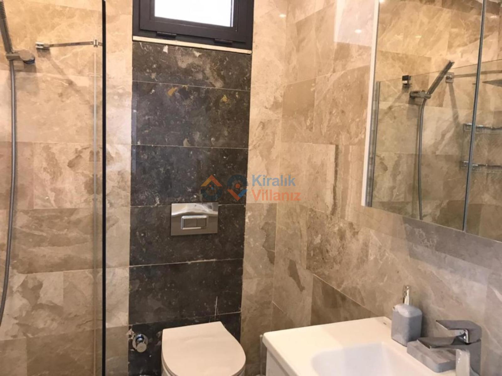 Bej mermer kaplı banyoda duşakabin ve lavabo.