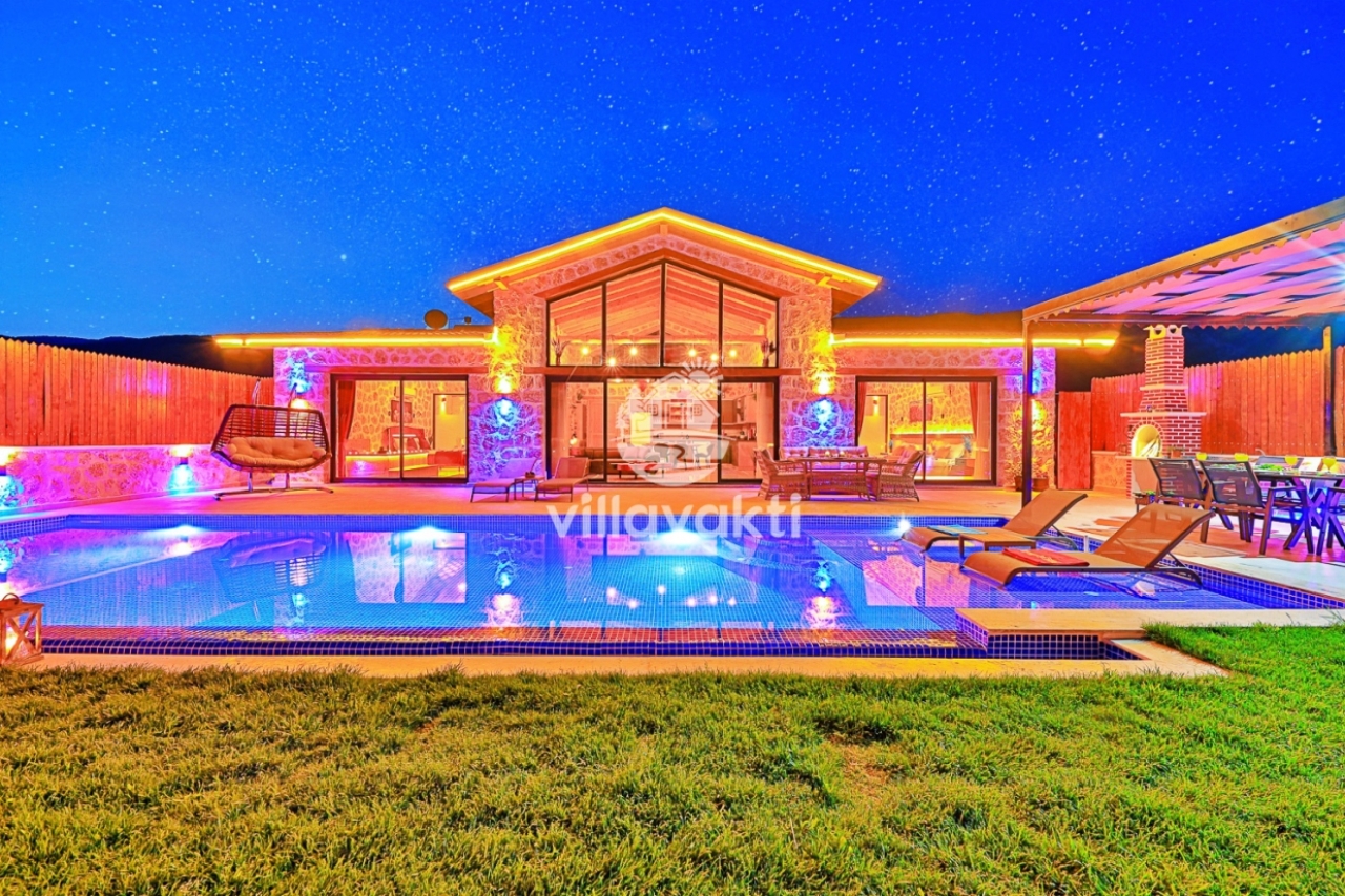 Aydınlatmalı havuzu ve şezlongları olan taş villa dış cephesi