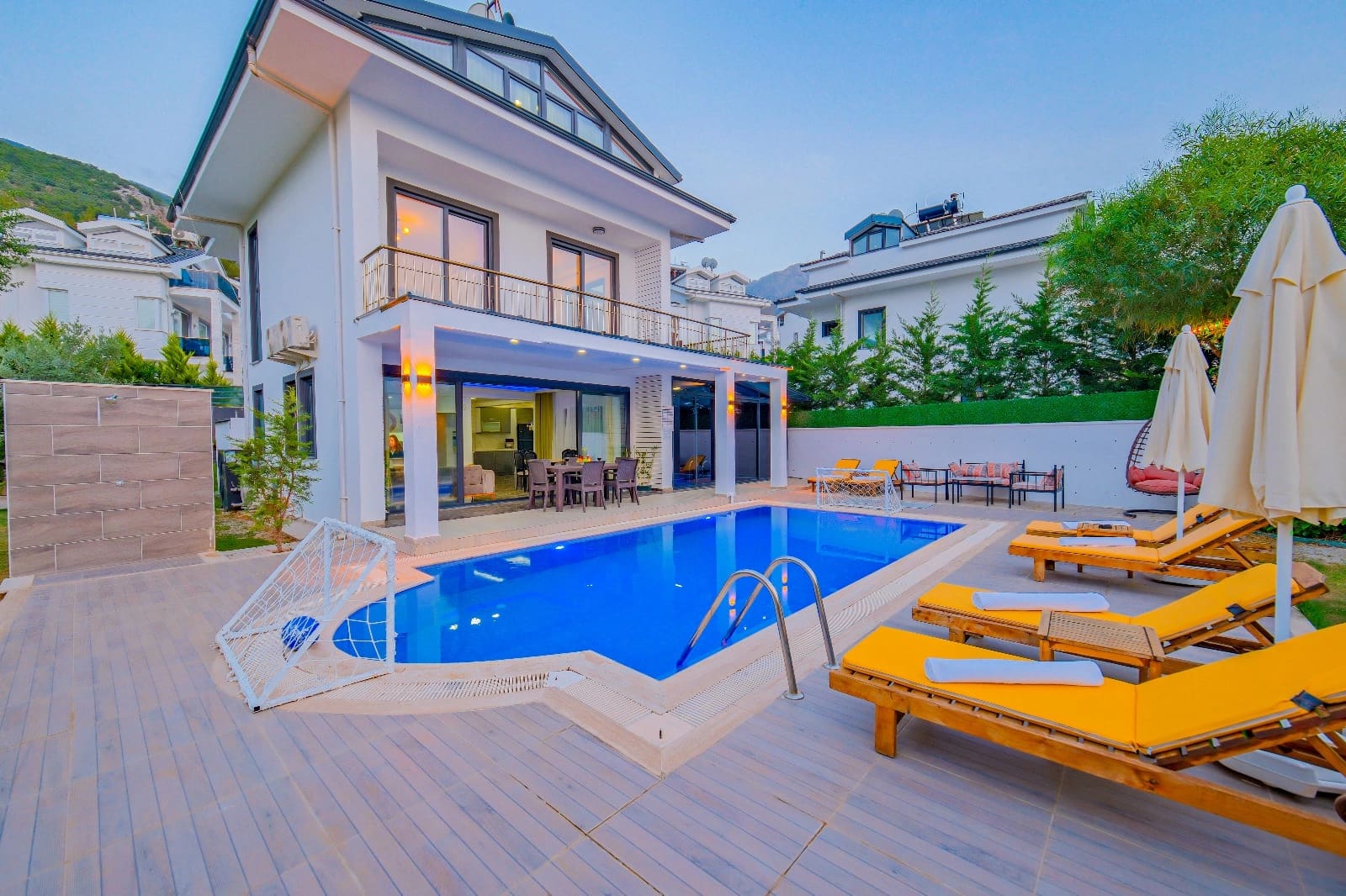 Önünde havuz, şezlonglar ve yemek masası olan iki katlı beyaz villa.