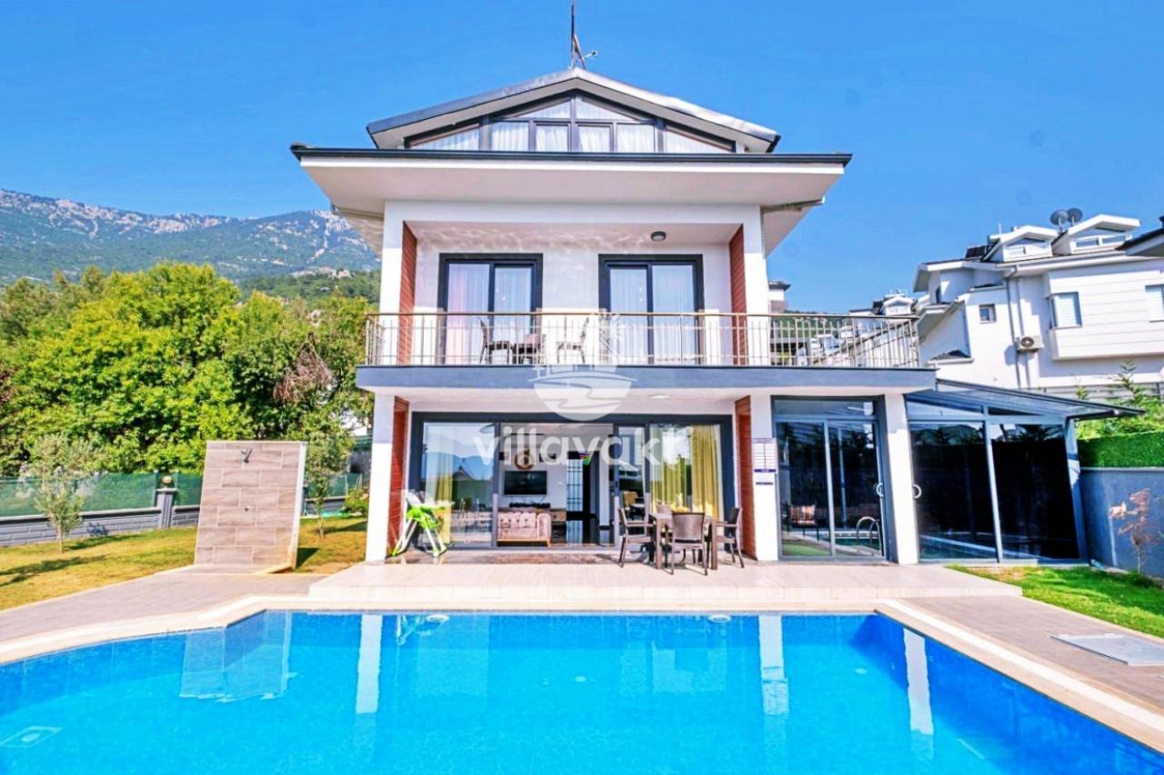 Önünde yüzme havuzu bulunan beyaz villa ve balkonundaki masa sandalyeler.