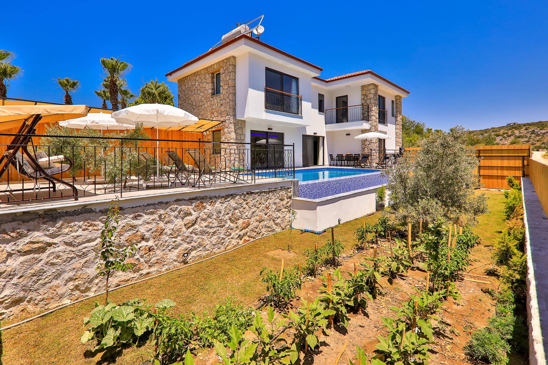 Bahçesinde ekili sebzeler ve havuzu bulunan beyaz taş villa.