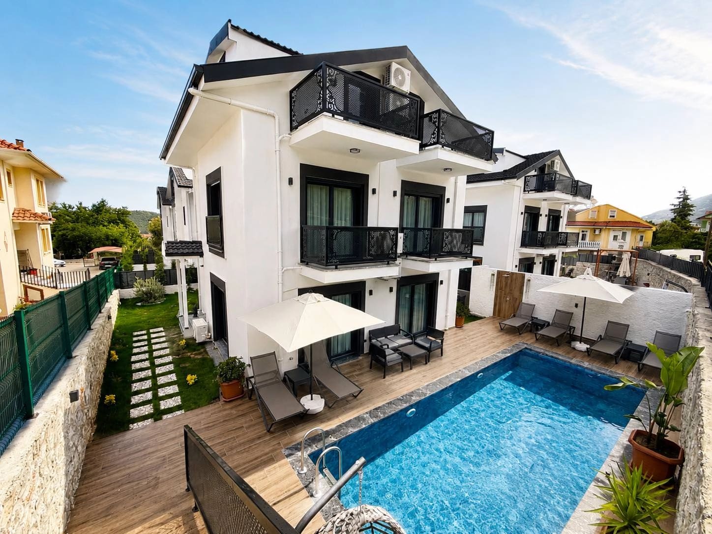 Bahçesinde yüzme havuzu ve şezlonglar bulunan beyaz villa.